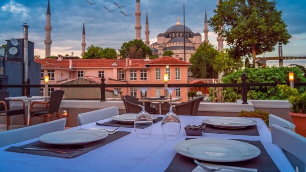 A rooftop dining area with tables set for two, overlooking a historic building with multiple minarets and a dome. - Sarnic Premier Hotel - Special Class (Istanbul)