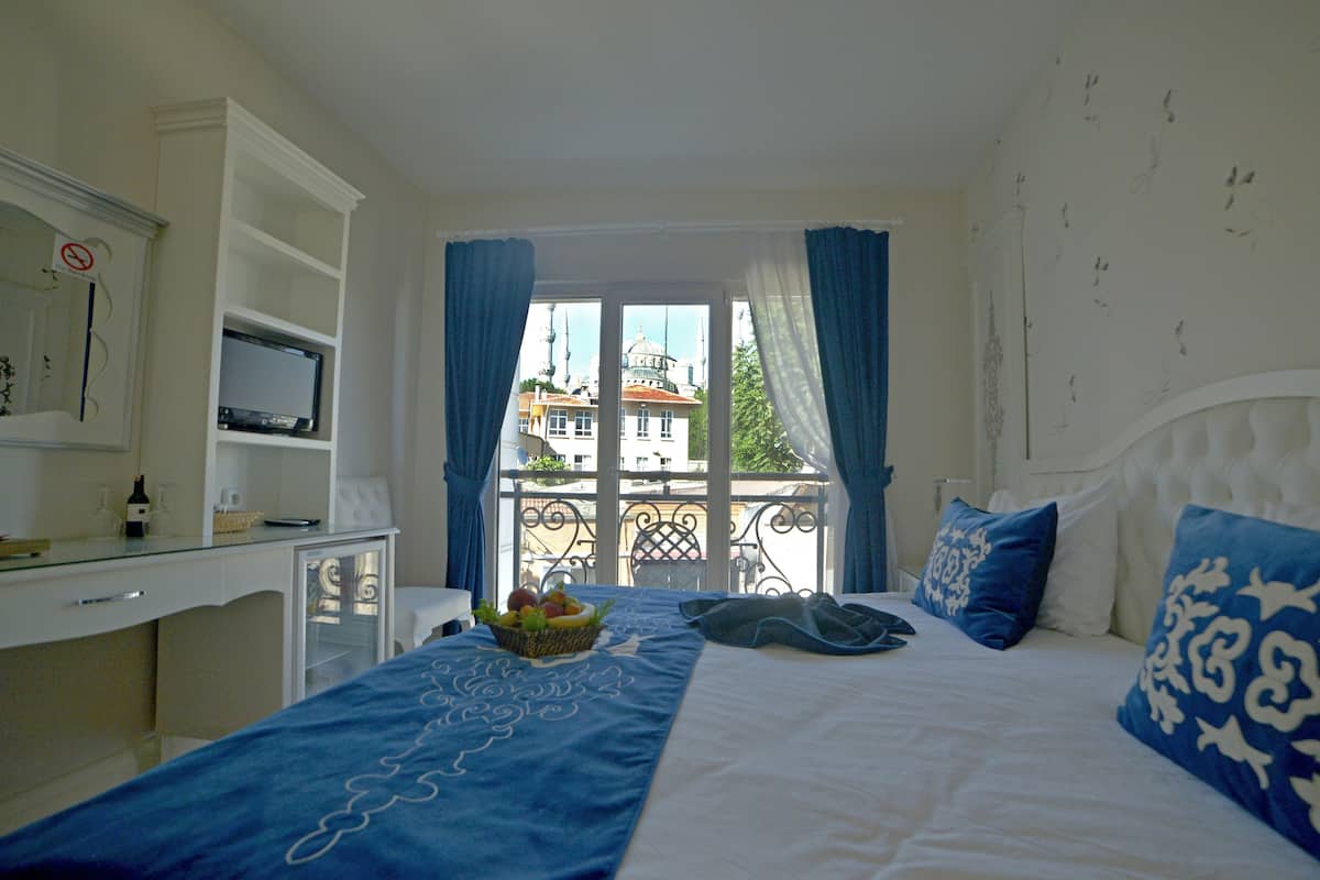 Une chambre avec un lit, un bureau, une télévision et un balcon donnant sur des immeubles.