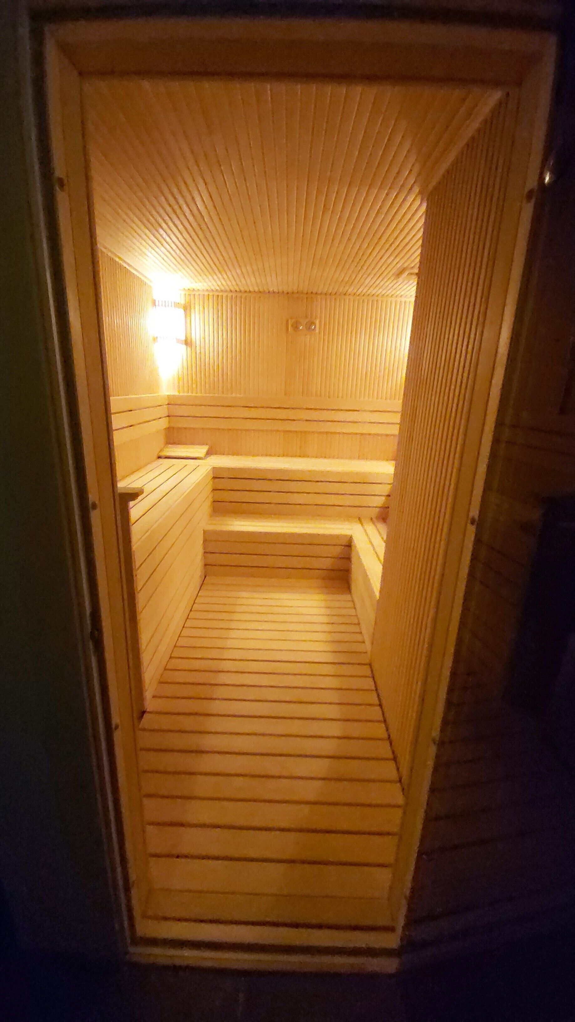 A sauna with wooden walls and benches, a sloped ceiling, and a visible light source.