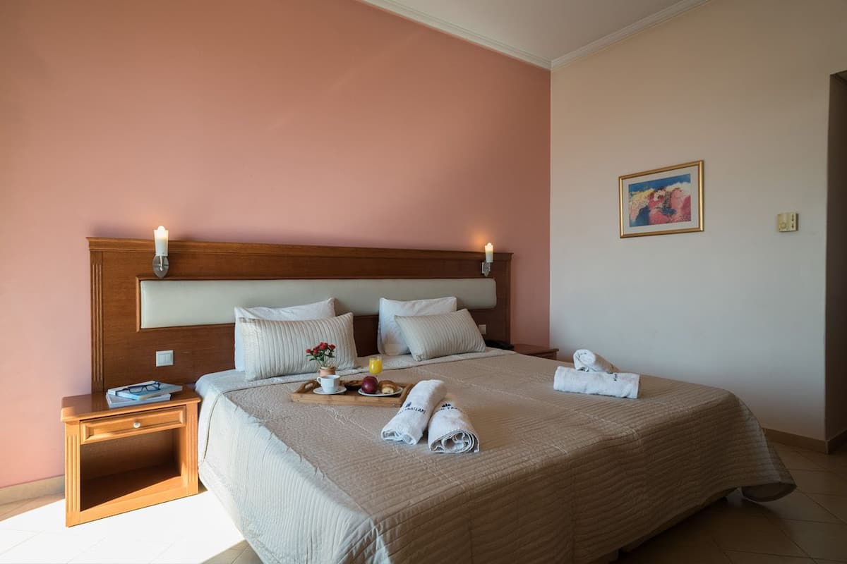 Ein ordentlich bezogenes Bett mit Holz-Kopfschild, ein Nachttisch mit einem Tablett mit Frühstücksgebäck, und ein Gemälde an der Wand.