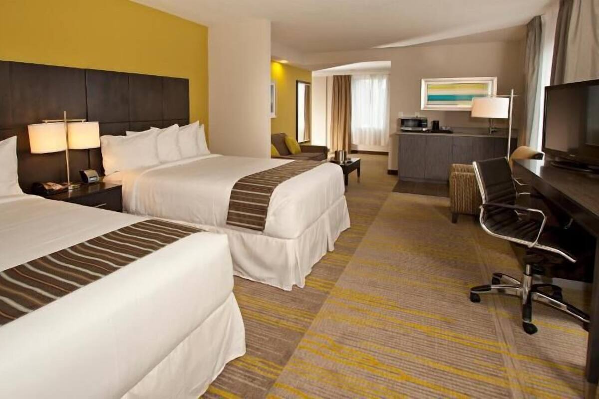 A hotel room with two beds, a desk, a chair, a television, and a kitchenette.