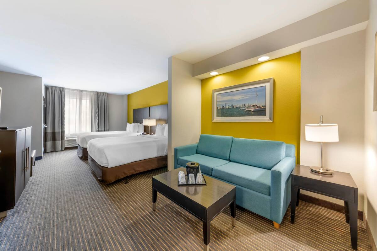 Habitación de hotel con dos camas, un sofá, una mesa de centro y un cuadro en la pared.