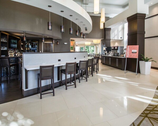 A modern bar area with a curved counter, bar stools, and hanging pendant lights.