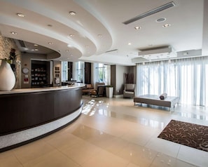 A modern hotel lobby with a curved reception desk, seating area, and large windows.