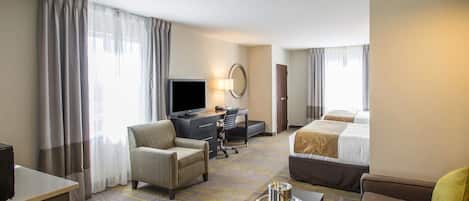 Una habitación de hotel con una cama, un escritorio con computadora, un televisor, un sofá y una mesa de centro.