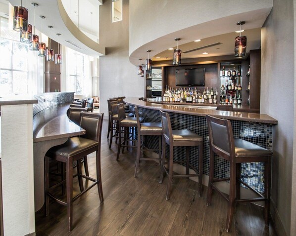 A bar area with wooden bar stools, a counter, and a television mounted above the bar. - Comfort Suites Miami Airport North (Miami Springs)