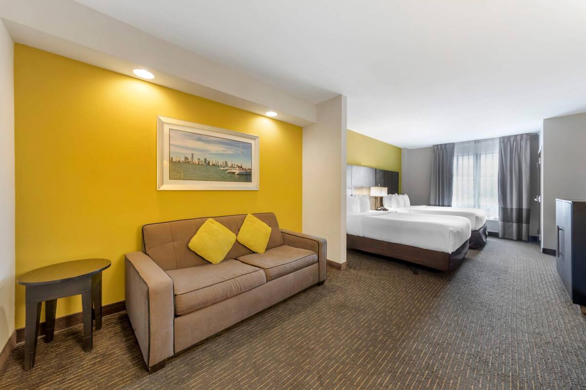 Habitación de hotel con sofá, dos camas, una mesita y un cuadro en la pared.