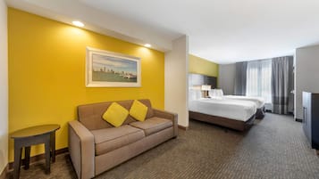 A hotel room with a sofa, two beds, a small table, and a painting on the wall.