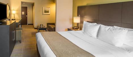 A hotel room with a large bed, a desk with a lamp, a television, and a chair.