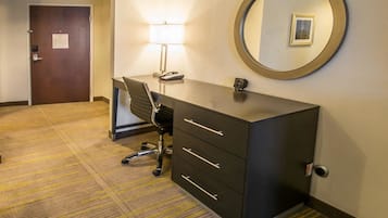 A hotel room with a desk, chair, and a large mirror on the wall.