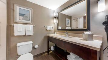 Un baño moderno con inodoro, lavabo y un espejo grande. Hay toallas colgadas en la pared y un cuadro sobre el lavabo.