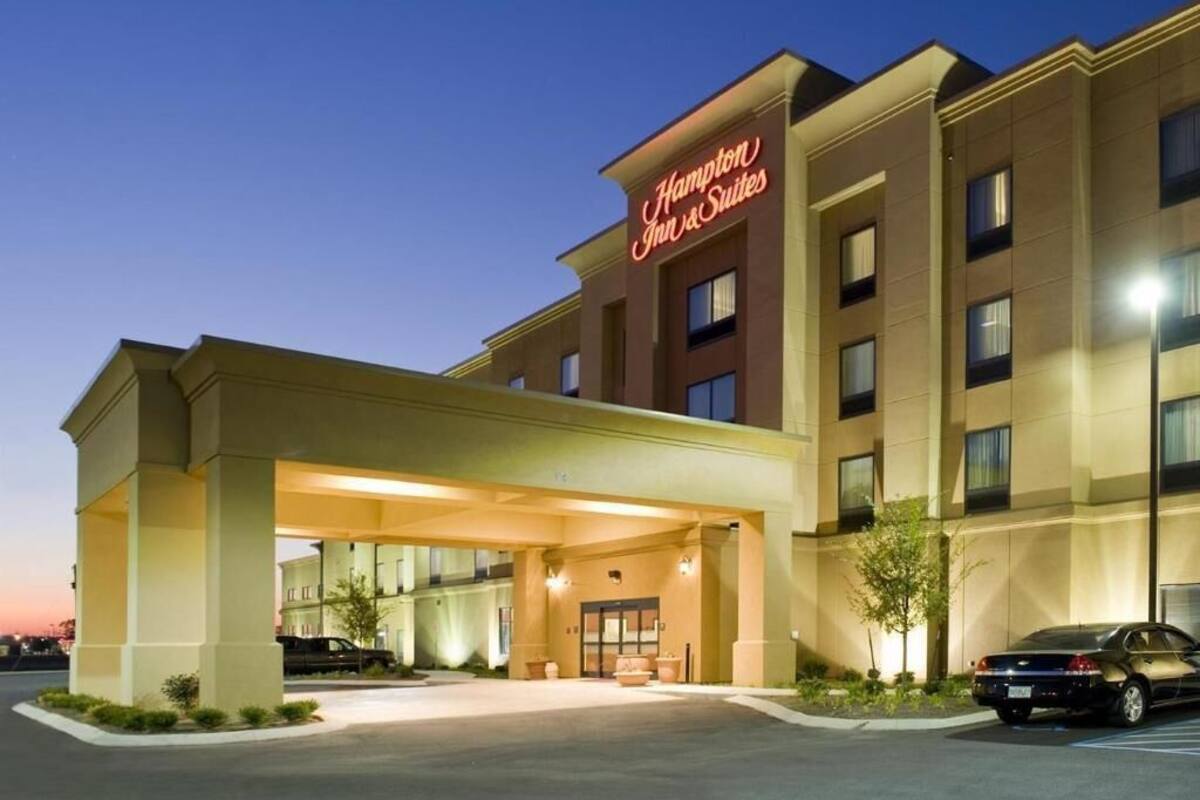 A Hampton Inn & Suites hotel with a covered entrance, multiple floors, and a parking lot.