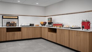 Een moderne keuken met houten kastjes, een witte tegelachtergrond en diverse apparaten, waaronder een koffiezetapparaat en een rode pan.