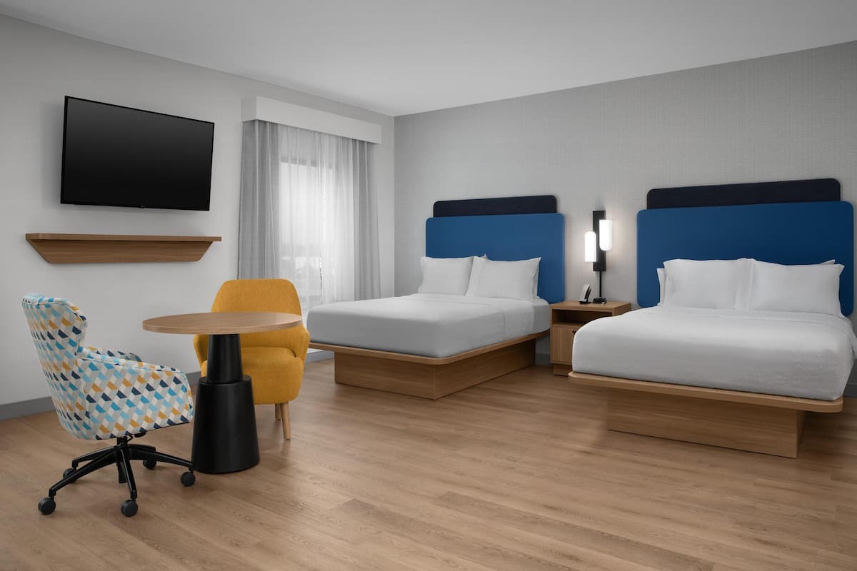 A hotel room with two beds, a TV, a desk, and a chair.