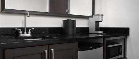 A modern kitchen with a black countertop, stainless steel sink, and a built-in coffee maker.