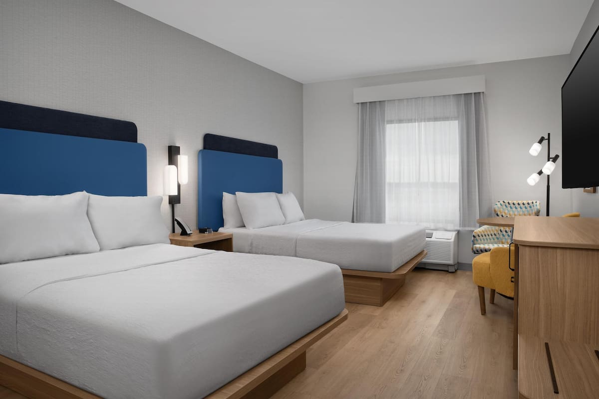 A hotel room with two beds, a desk, a chair, a TV, and a window with curtains.