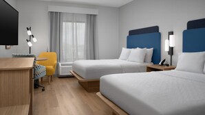 Een hotelkamer met twee bedden, een bureau, een stoel, een televisie en een raam met gordijnen.