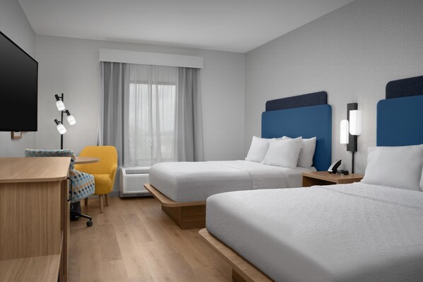 A hotel room with two beds, a desk, a chair, a TV, and a window with curtains.