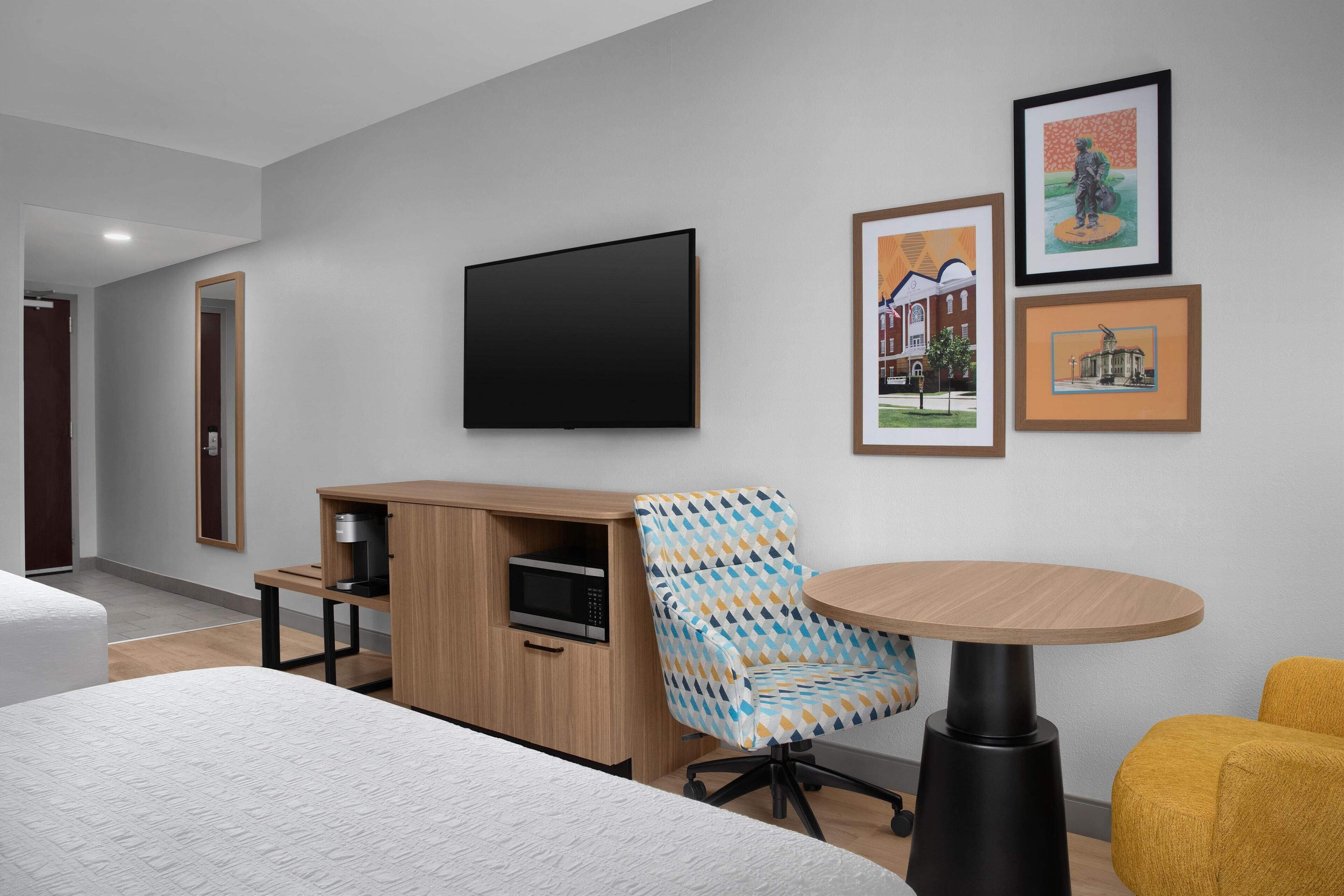 Quarto de hotel moderno com uma cama grande, uma escrivaninha de madeira, uma televisão e quadros na parede.