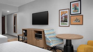 Quarto de hotel moderno com uma cama grande, uma escrivaninha de madeira, uma televisão e quadros na parede.
