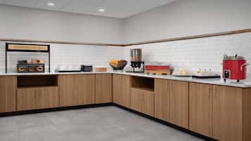 Una cucina moderna con mobili in legno, zoccolo paraschizzi in piastrelle bianche e diversi elettrodomestici, tra cui una macchina da caffè e una pentola rossa.