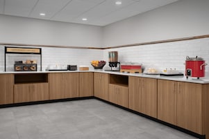 Una cocina moderna con armarios de madera, salpicadero blanco de azulejos y diversos electrodomésticos, incluyendo una cafetera y una olla roja.