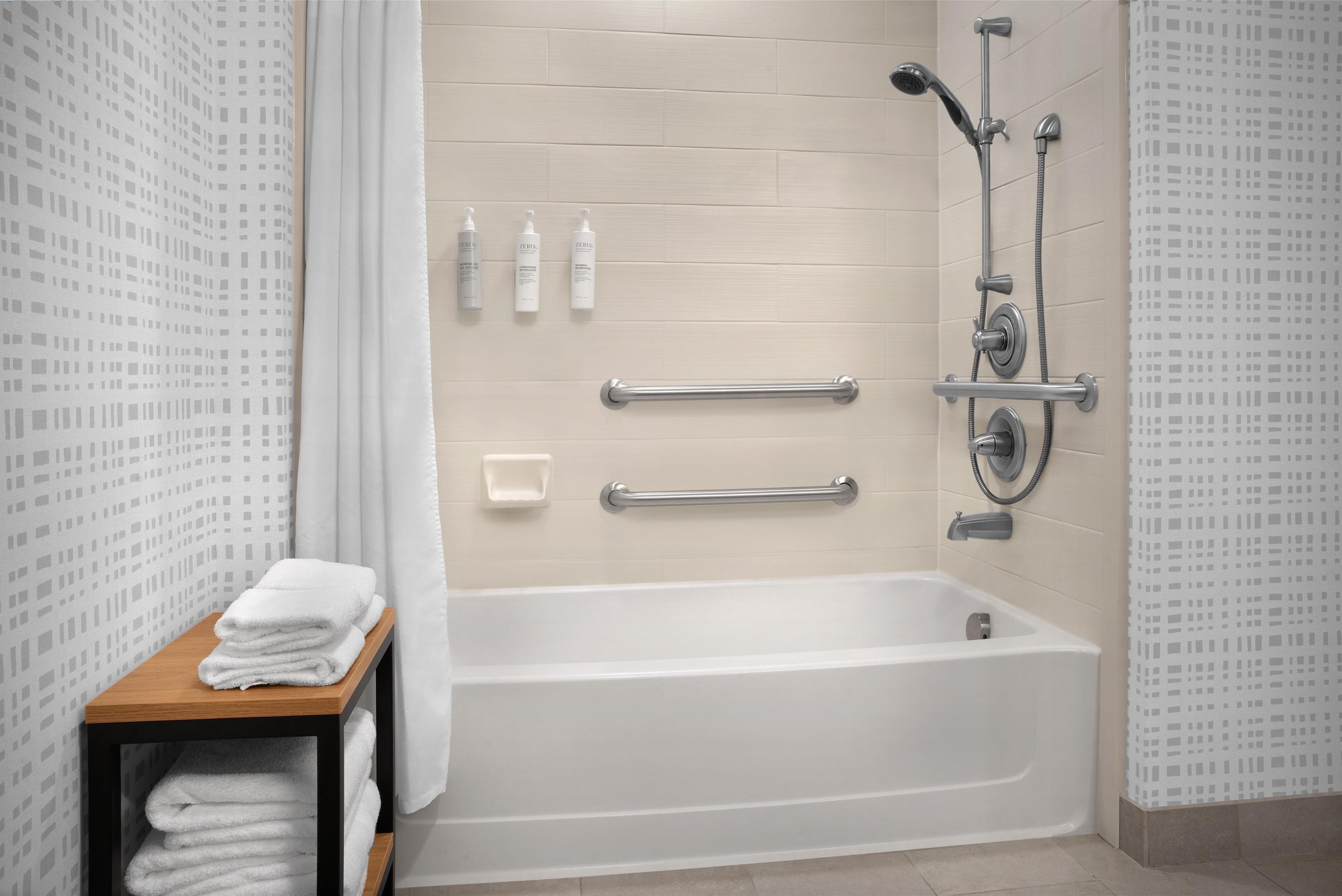 Une salle de bain moderne avec une baignoire, des barres d’appui et une étagère avec des serviettes.