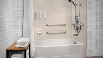 Une salle de bain moderne avec une baignoire, des barres d’appui et une étagère avec des serviettes.