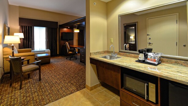 A hotel room with a kitchenette, a sofa, a chair, a TV, and a large mirror. - Hampton Inn Geneseo (Geneseo)