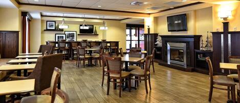 A spacious dining area with multiple tables and chairs, a fireplace, and a television mounted on the wall.