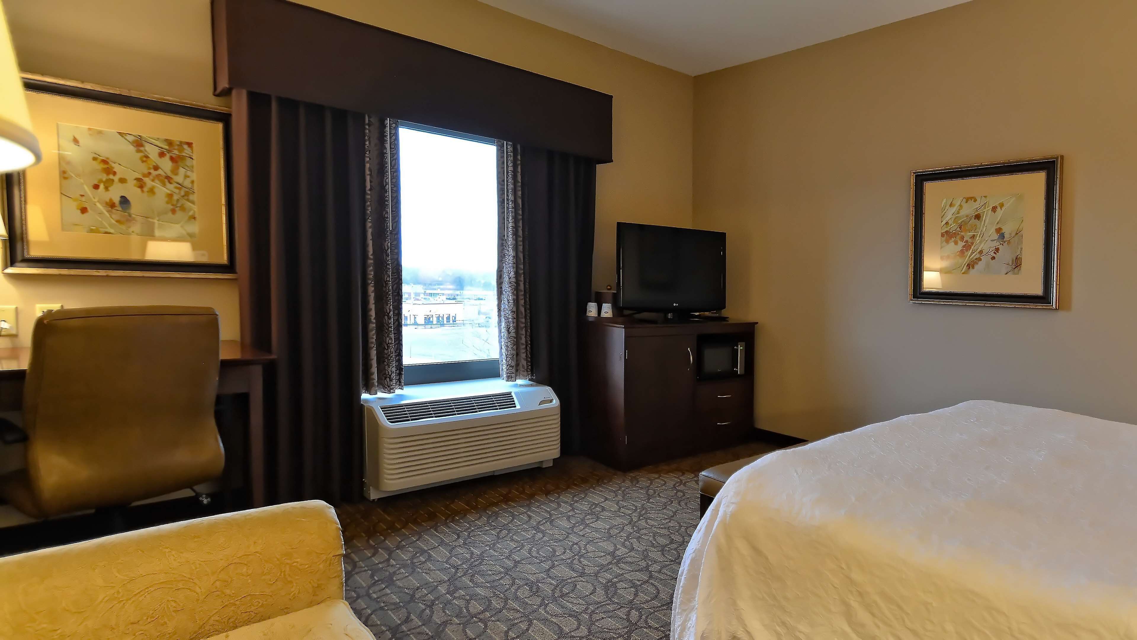A hotel room with a bed, a desk, a chair, a television, and a window with curtains.