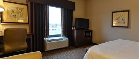 A hotel room with a bed, a desk, a chair, a television, and a window with curtains.