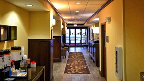 A hotel lobby with a wooden floor, a reception desk, a coffee station, and a view of the outside through large windows. - Hampton Inn Geneseo (Geneseo)
