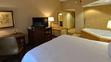 A hotel room with a bed, a desk with a television, a chair, a bathroom with a bathtub, and a framed picture on the wall.
