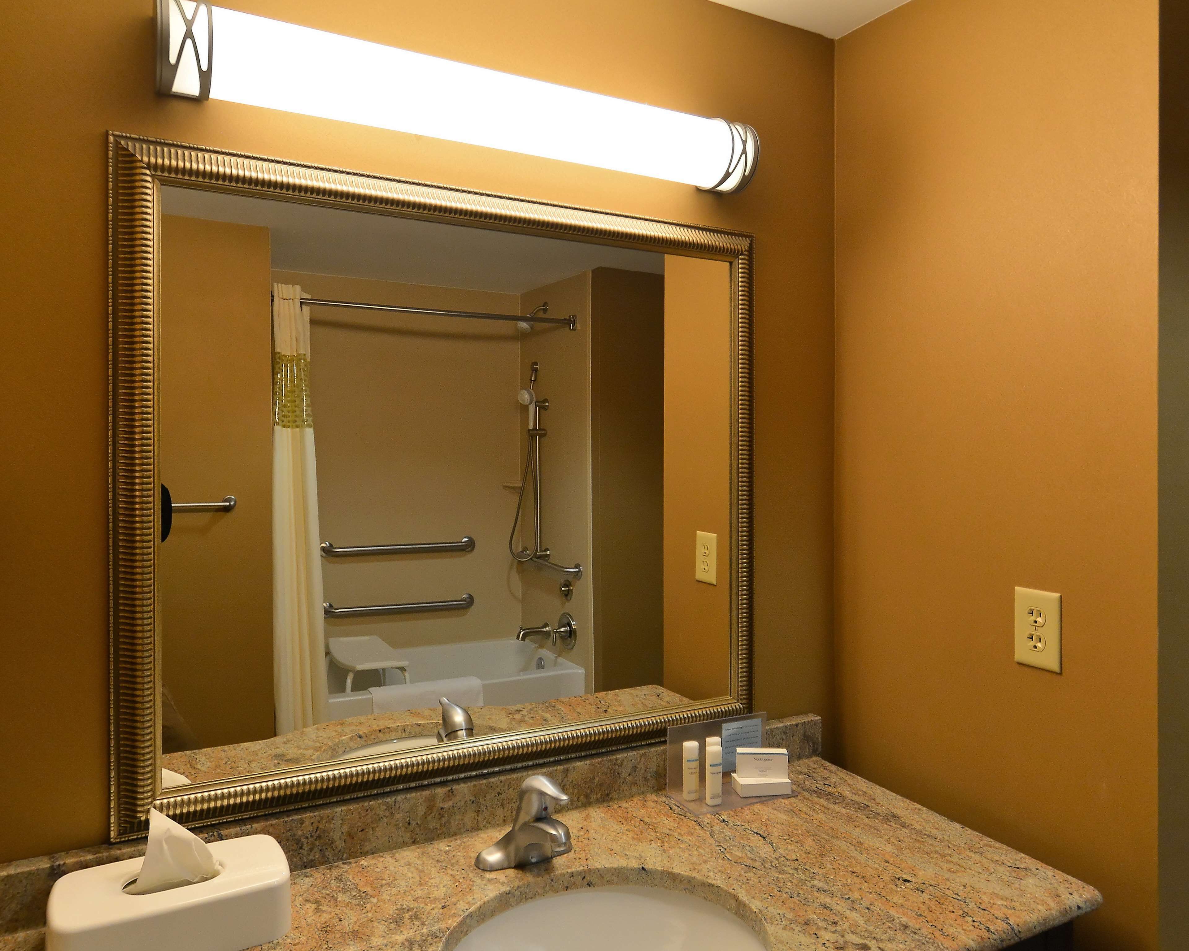 Une salle de bain avec un grand miroir, un lavabo, un distributeur de serviettes et un espace douche.