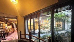 A hotel lobby with a wooden railing, a carpeted floor, and a view of an indoor garden through large windows. - Ishicho (Kyoto)