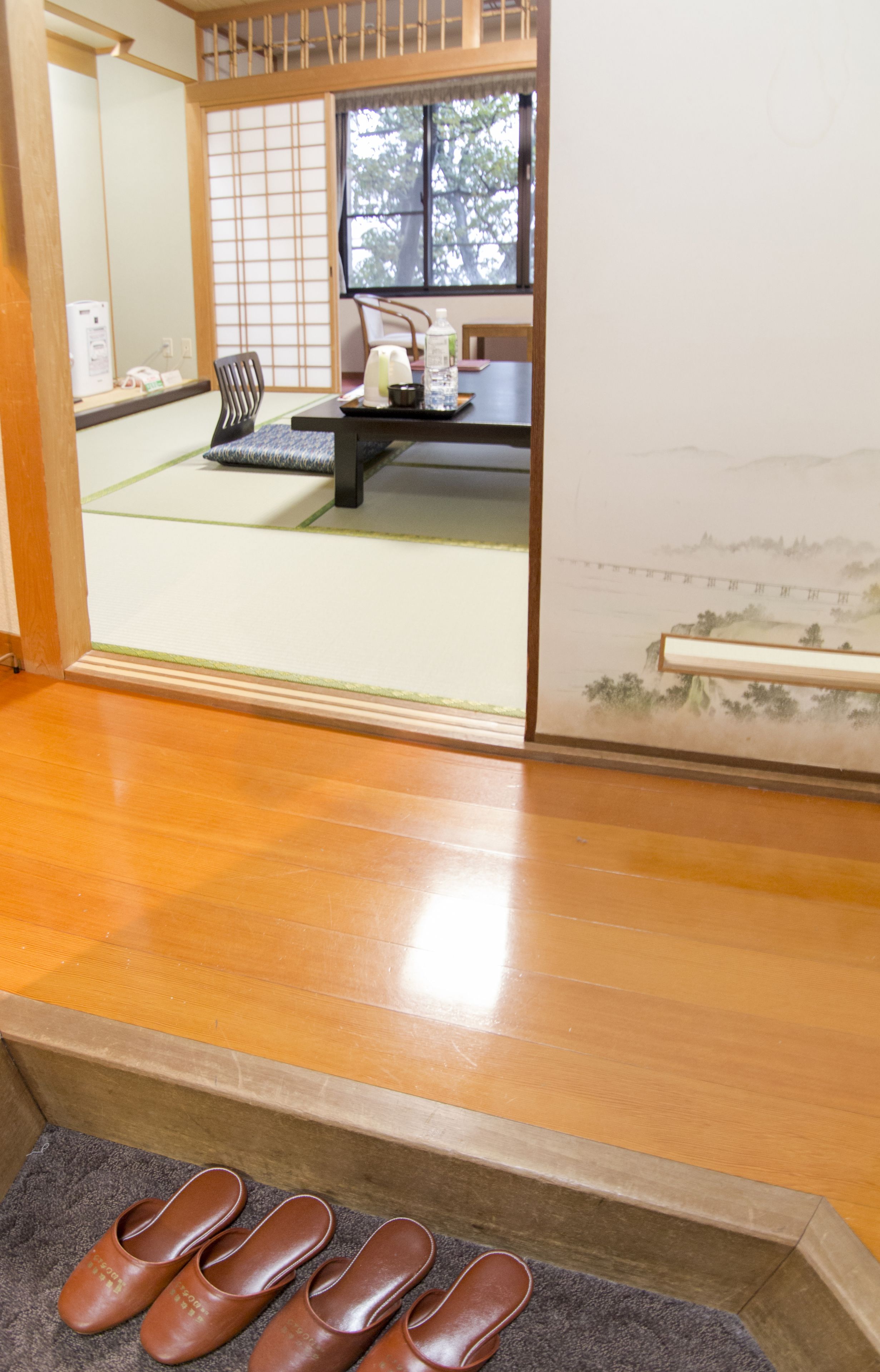 A traditional Japanese room with tatami flooring, a shoji screen, and a view of a bridge through the window.