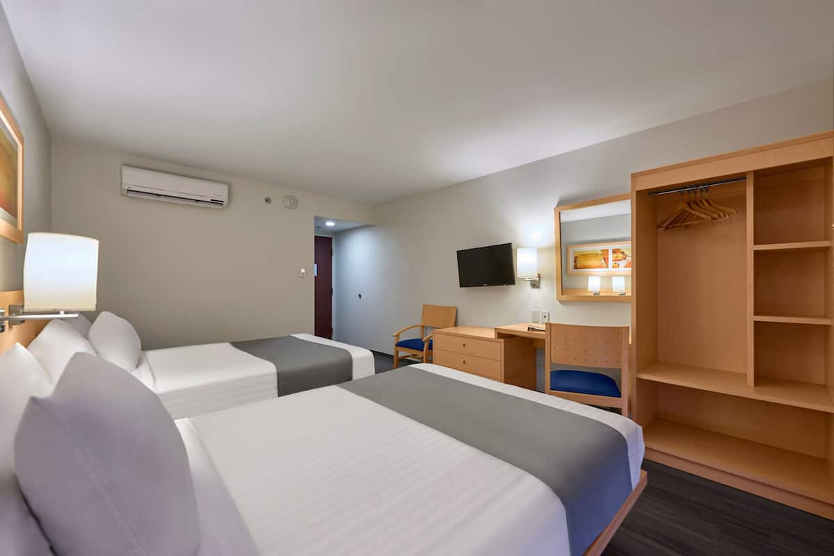 A hotel room with two beds, a desk, a chair, a wardrobe, and a TV.