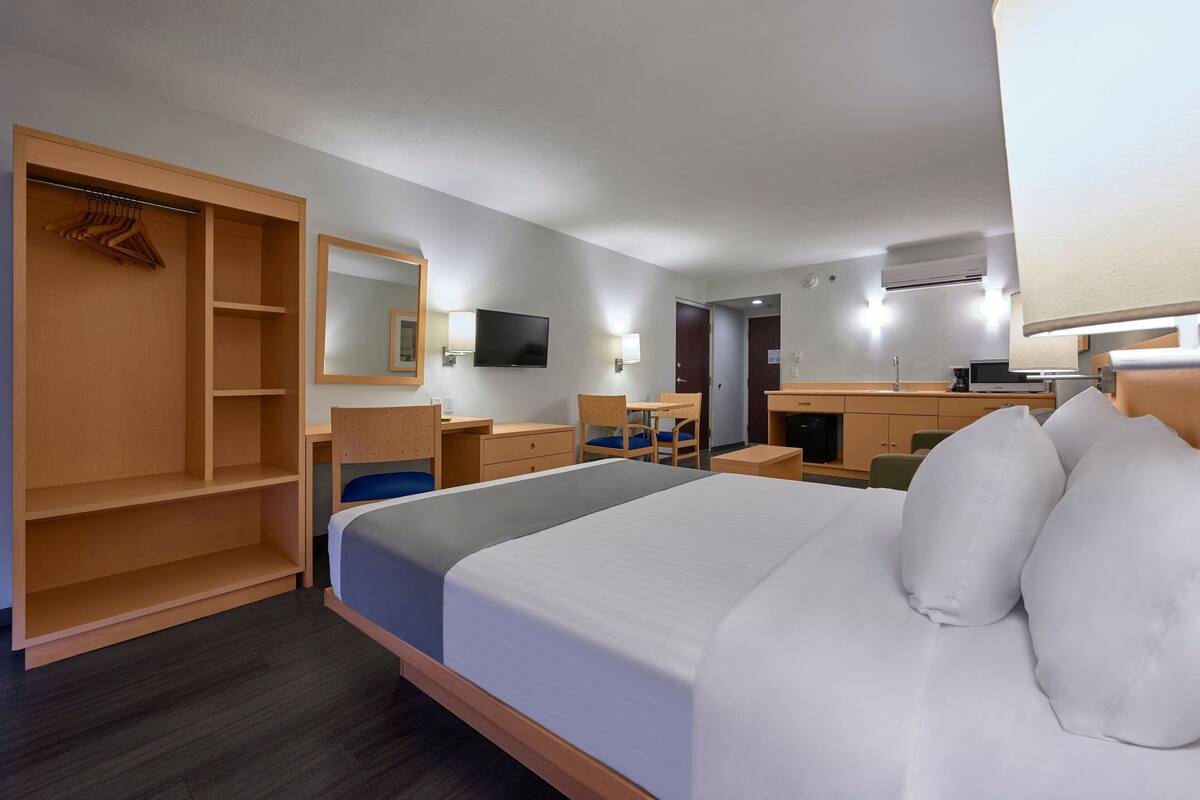 A hotel room with a large bed, a desk, a chair, a wardrobe, and a TV.