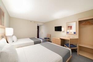 Habitación de hotel con dos camas, un escritorio, una silla, un televisor, un espejo y un armario.