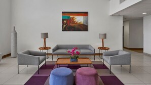 Un salon moderne avec un canapé gris, deux fauteuils, une table basse ornée d’un vase de fleurs et deux poufs.