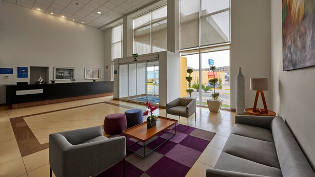 Un hall d’entrée moderne doté d’un comptoir de réception, d’un espace salon et de grandes fenêtres offrant une vue sur l’extérieur.