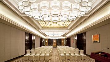A spacious conference room with rows of white chairs, a patterned carpet, and a ceiling with multiple chandeliers.