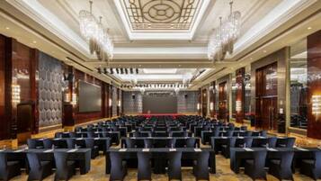 A conference room with rows of chairs, a stage, and a large screen.