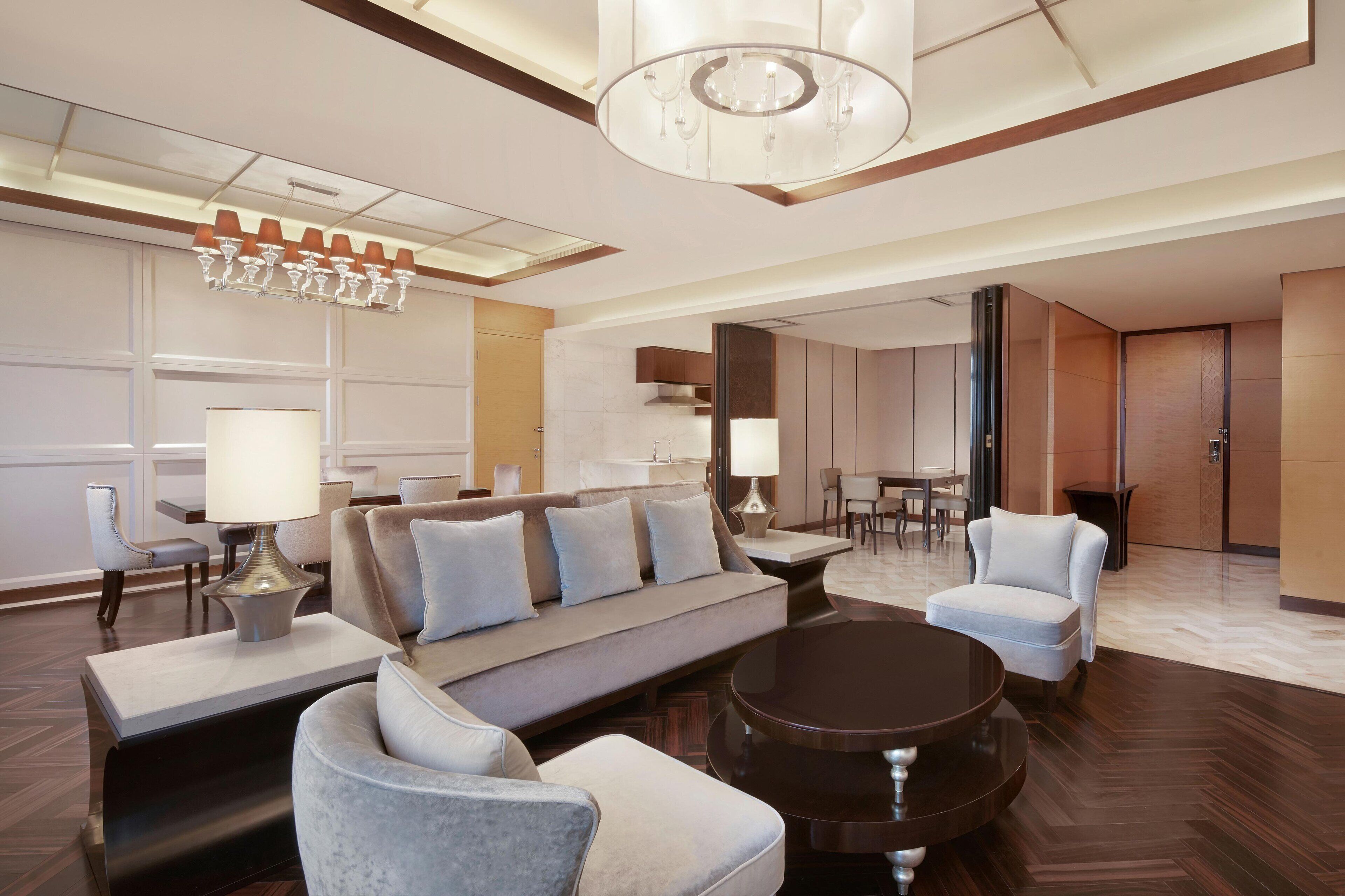 A spacious hotel lobby with a modern design, featuring a large sofa, armchairs, a coffee table, and a chandelier.