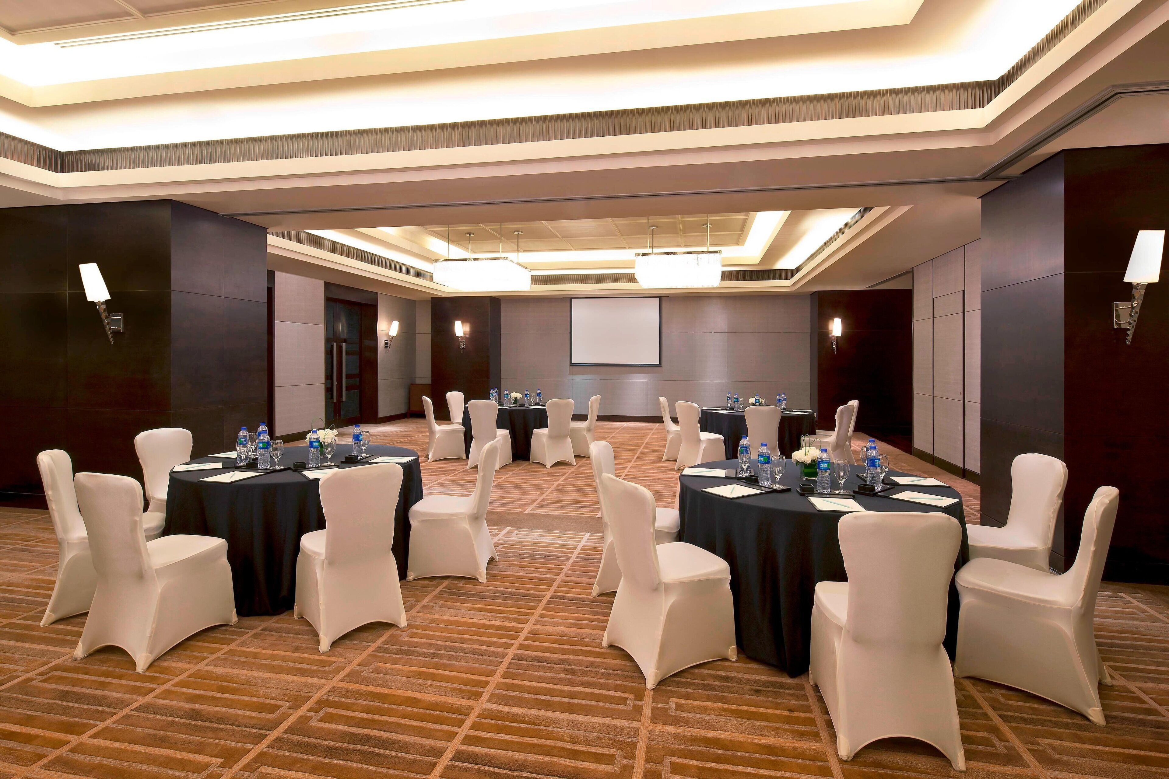 Un salón de conferencias con varias mesas y sillas, equipado con botellas de agua y tarjetas de identificación, en un entorno moderno y bien iluminado de un hotel.
