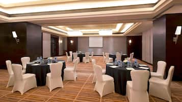 A conference room with multiple tables and chairs, equipped with water bottles and nameplates, in a well-lit, modern hotel setting.