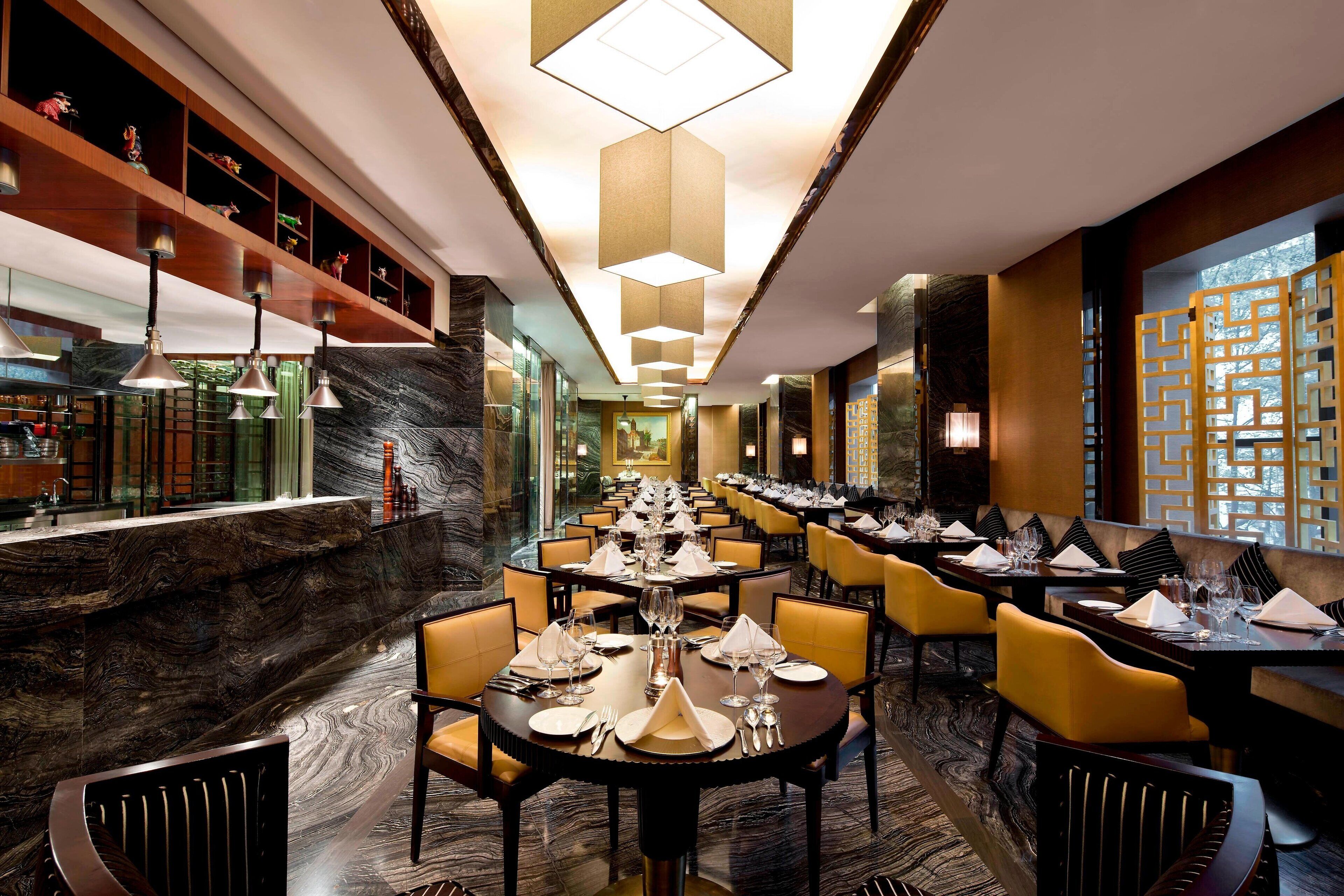 A restaurant with a long counter, multiple tables set for dining, and a decorative ceiling.