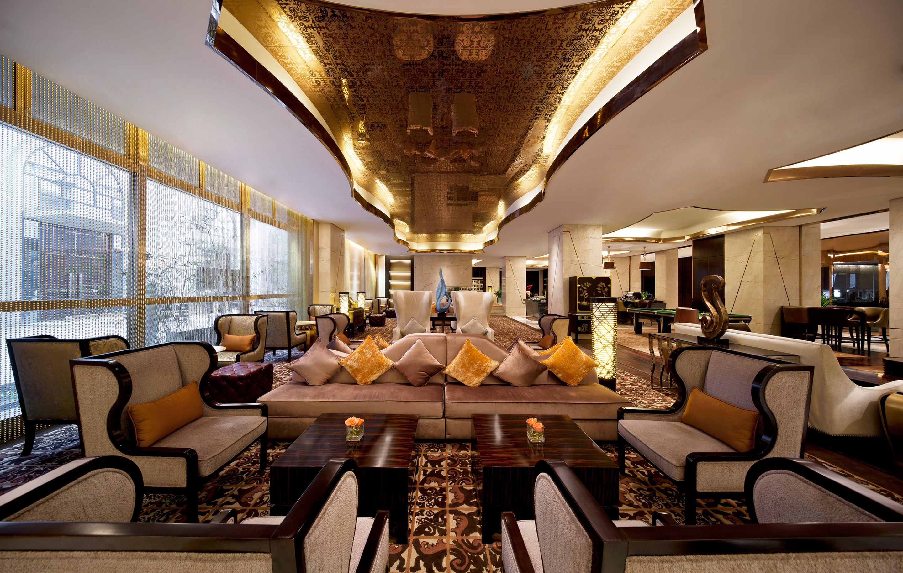 Een ruime lobby met een centraal zithoek, grote ramen en een hoog plafond met ingewikkelde decoraties.