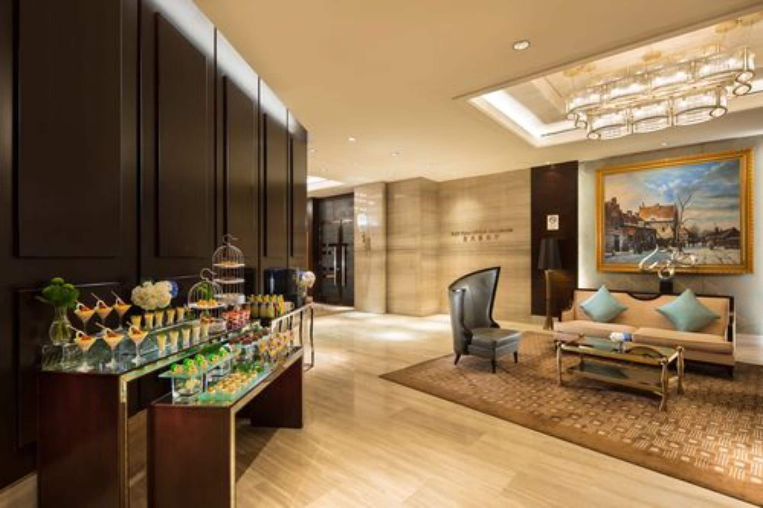 A modern hotel lobby with a reception desk, a seating area with a sofa and armchairs, and a large painting on the wall.